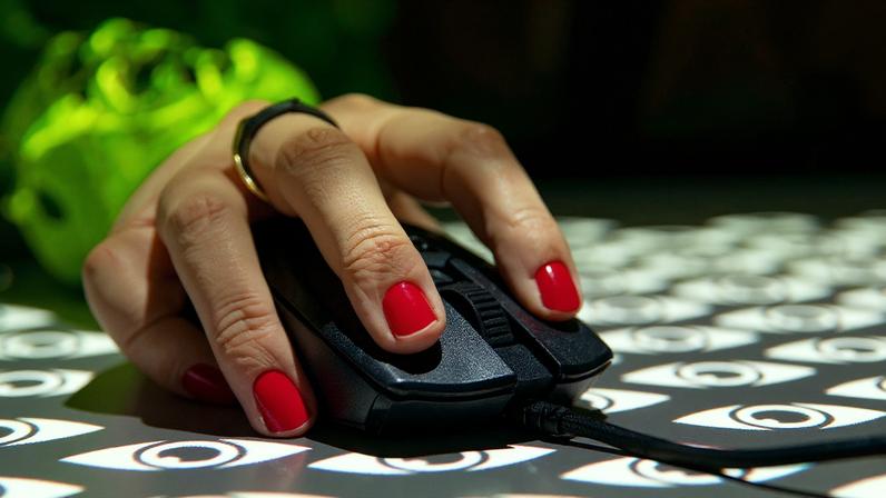 Photograph of a hand wearing red nail varnish holding a mouse with a projection overlay of stylized eyes