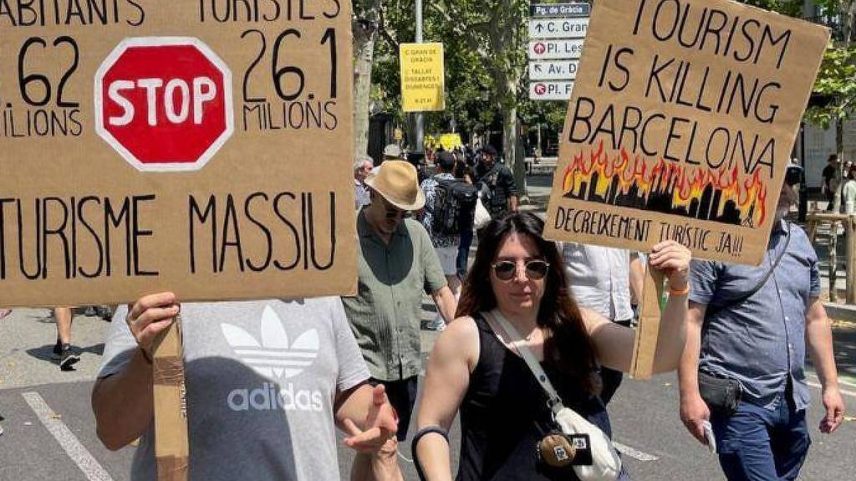 Pessoas caminham pelas ruas de Barcelona, na Espanha, portando cartazes contra o turismo em massa na cidade "O seu AirBnB era a minha casa", diz o cartaz em catalão (Foto: BBC)