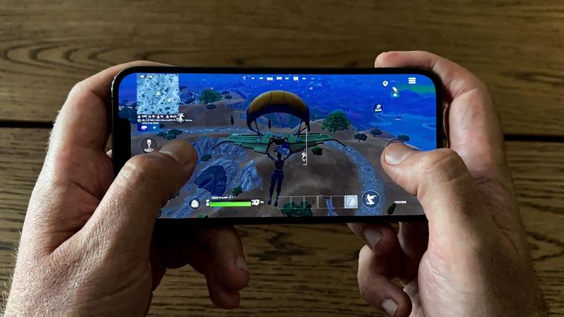 An iPhone being held with two hands playing Fortnite.