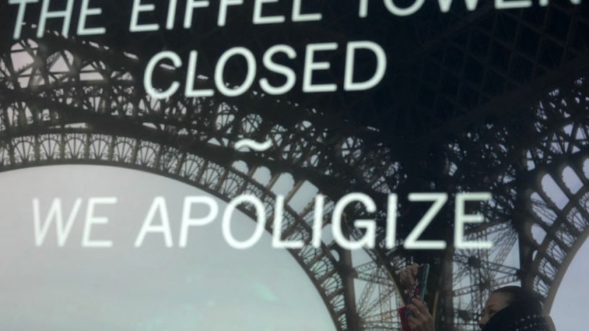 A fotografia tirada em 27 de dezembro de 2023 em Paris mostra o reflexo de um turista e da Torre Eiffel em um painel informando os visitantes que o local está fechado após a greve dos funcionários. (Foto: AFP via Getty Images)