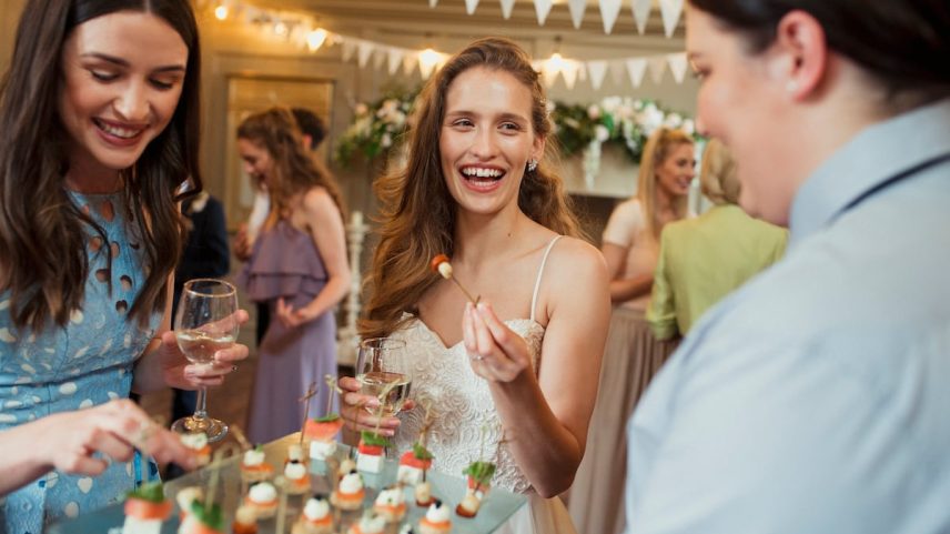 Uma noiva sorri enquanto pega um canapé no coquetel de seu casamento. (Foto: Getty Images)