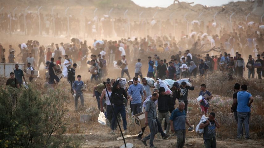 Palestinos carregam suprimentos da Fundação Humanitária de Gaza (GHF), um grupo privado apoiado pelos EUA que substituiu o antigo sistema liderado pela ONU, perto de centro de distribuição no centro do enclave. 08/06/2025 (Foto: Eyad Baba/AFP)