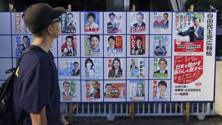 Um pedestre observa cartazes dos candidatos do Partido Liberal Democrata (PLD) e de Shigeru Ishiba, à direita, em Tóquio, 20 de julho (Foto: Bloomberg)