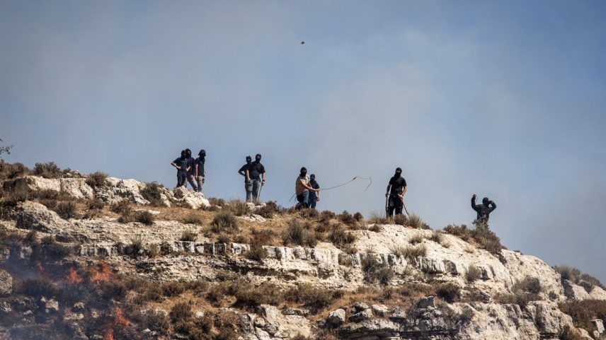 Colonos israelenses mascarados atiram pedras em palestinos do topo de uma colina na vila de Sinjil, na Cisjordânia ocupada, em 4 de julho (Foto: John Wessels/AFP)