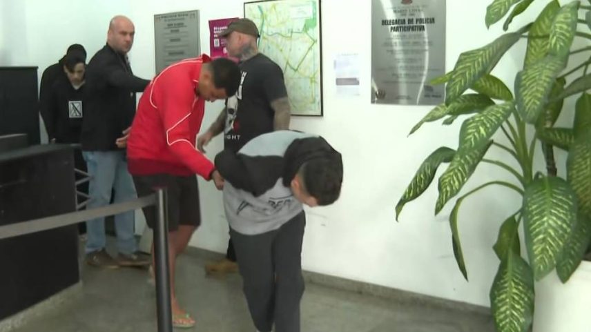 Suspeitos escondem os rostos ao chegar à delegacia (Foto: Reprodução TV Globo)