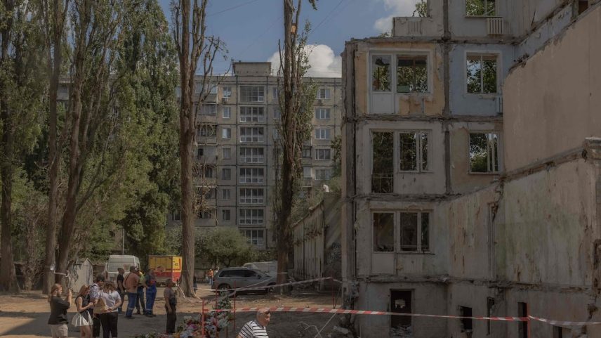 Pessoas se reúnem ao lado de flores, brinquedos infantis e retratos colocados em memória das vítimas no local de um prédio residencial de nove andares destruído após um recente ataque com mísseis russos em Kiev, em 5 de agosto de 2025 (Foto: Roman Pilipey/AFP)