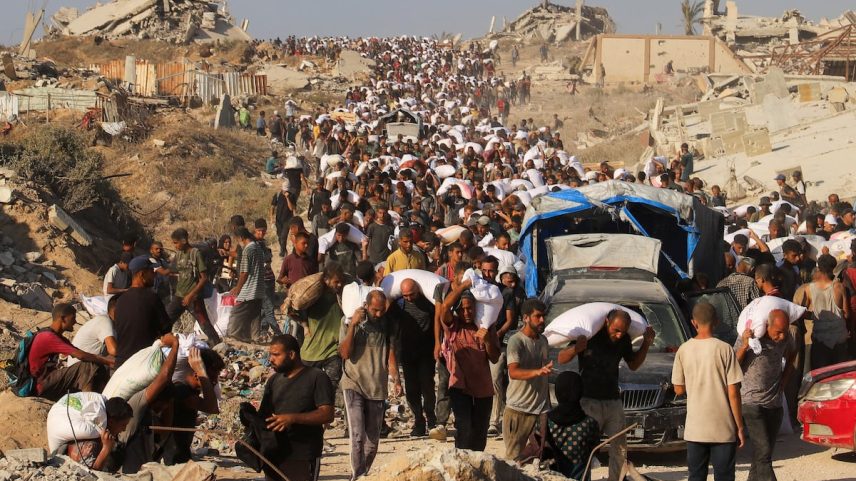 Centenas de gazatíes carregam neste domingo a ajuda que conseguiram em Beit Lahia. (Foto: Ebrahim Hajjaj/REUTERS)