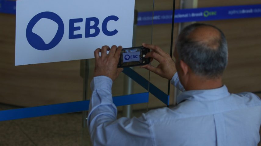 Homem fotografa a nova marca da Empresa Brasil de Comunicação (EBC), na entrada da empresa, em Brasília (Foto: José Cruz/Agência Brasil)