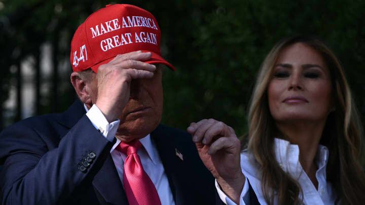Primeira-dama Melania Trump (C) observa enquanto o presidente dos EUA, Donald Trump, coloca seu chapéu MAGA antes de cumprimentar membros das forças armadas e suas famílias durante o Piquenique da Família Militar no Jardim Sul da Casa Branca em Washington, DC, em 4 de julho de 2025. (Foto: Brendan Smialowski | Afp | Getty Images)
