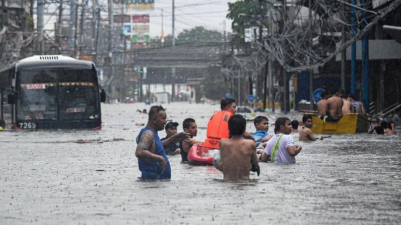 Pessoas atravessam as águas da enchente (Foto: Ted ALJIBE / AFP)
