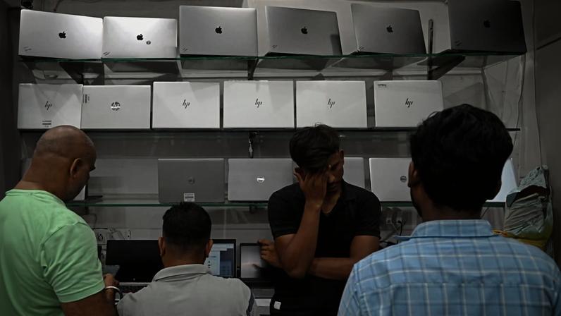 Four men are standing in front of a display of silver laptops.