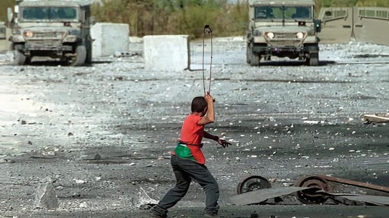 A Palestinian demonstrator uses a slingshot to throw stones at IDF vehicles on the outskirts of Ramallah, West Bank, September 2001.
