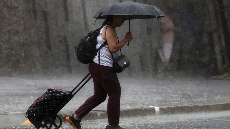 A woman wheeling a trolley and holding an umbrella walks in torrential rain