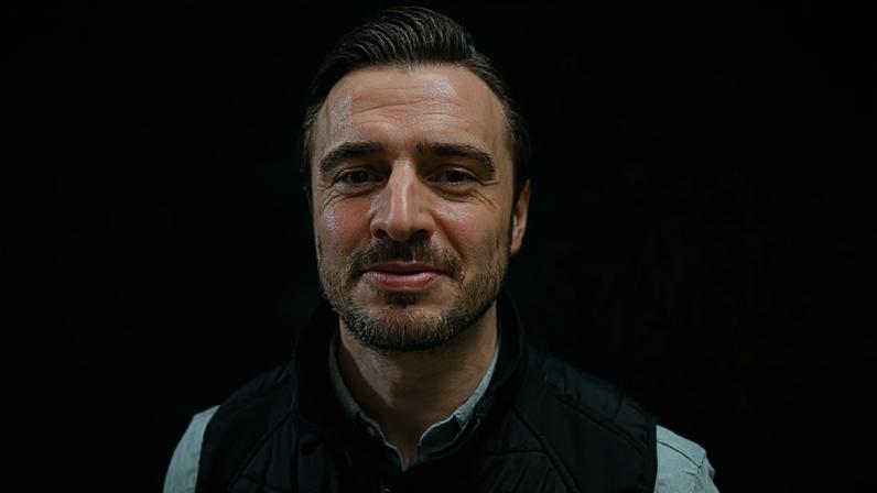 A man in a black puffer jacket and grey top