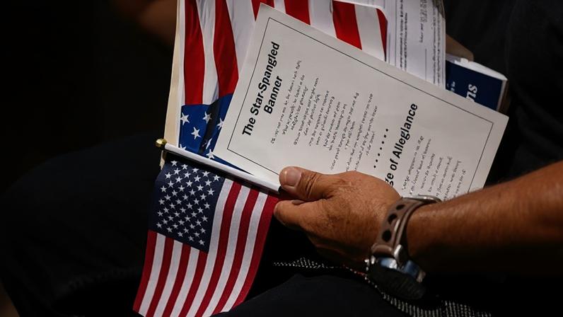 An attendee holds the US flag and the lyrics of the Star-Spangled Banner during a naturalization ceremony in Mount Vernon, Virginia, on 4 July 2025.