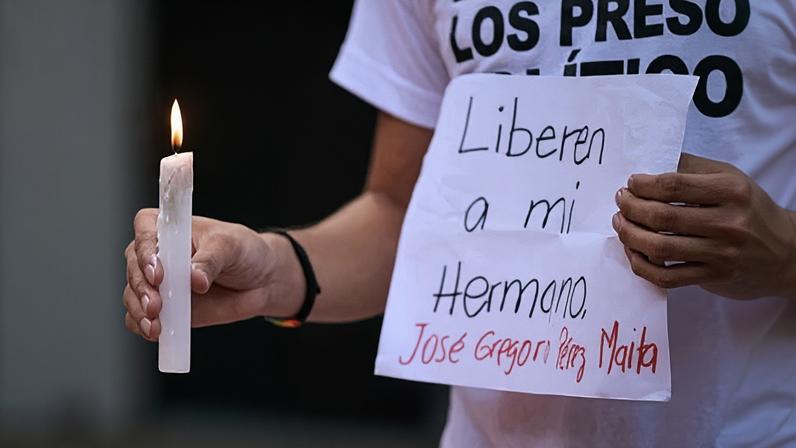 A man holds a candle and a sign asking for the release of his brother during a vigil for political prisoners in Caracas, Venezuela, on 8 August 2024.