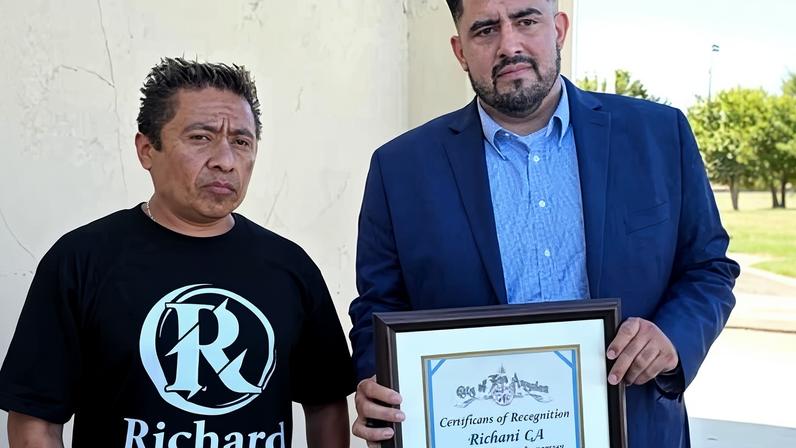 In this photo provided by the office of city council member Curren Price, Carlitos Ricardo Parias receives a certificate of recognition from Jose Ugarte, Price’s chief of staff, in August.