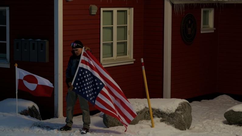 A person carries an American flag upside down in front of the U.S. Consulate in Greenland as a form of protest.