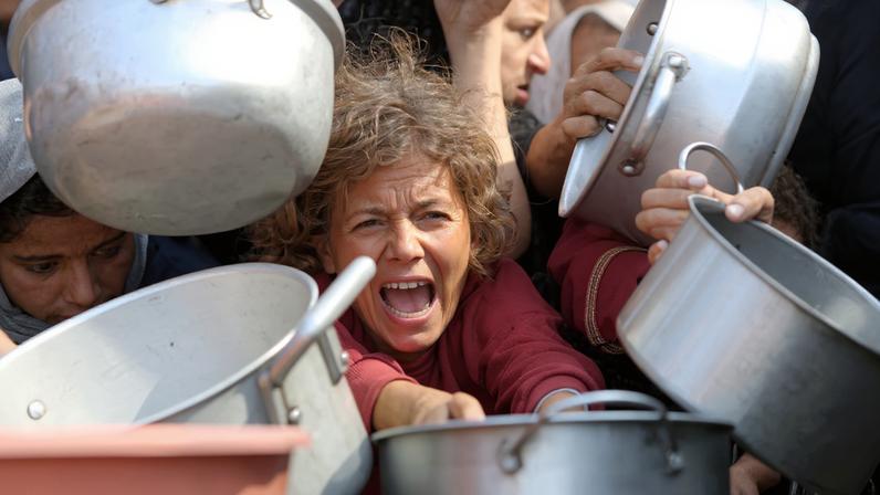 A child reacts surrounded by pots as Palestinians wait to receive food from a charity kitchen in Khan Younis