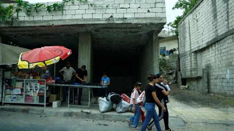 Women walk past a street stall in the countryside of Latakia