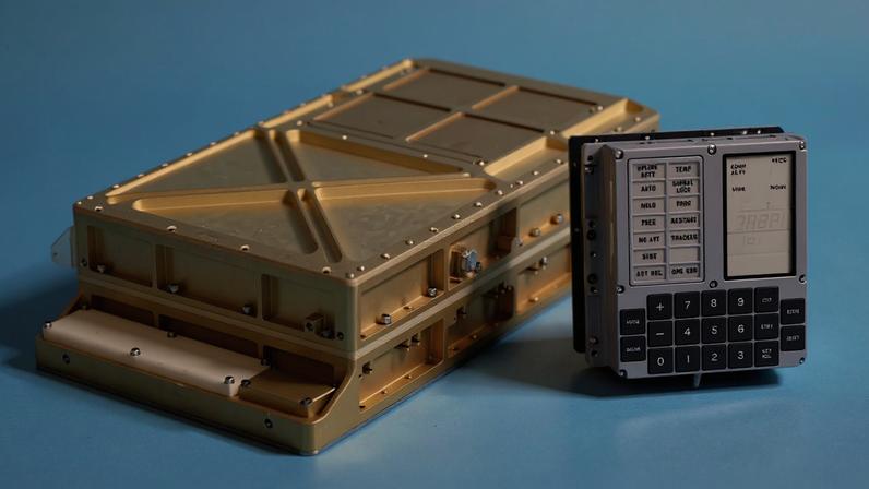 Imagem, em fundo azul, do computador de bordo da Apollo 11. Vê-se um hard disc e um painel de controle.