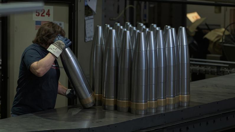 An employee handles large shells at an ammunition manufacturing plant.