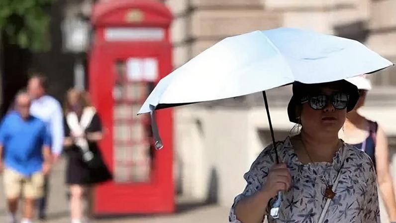 EPA A woman, wearing a sunhat and sunglasses, holds an umbrella to shade herself as she walks along a street in London. There is a red telephone box behind her as well as a few other pedestrians.