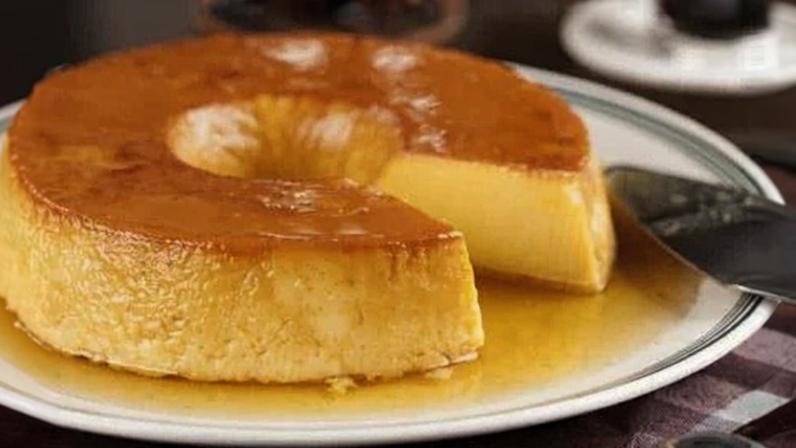 Pudim servido em prato branco com um pedaço cortado em cima de mesa de madeira