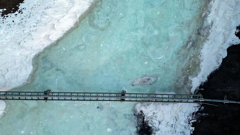 An aerial view of an oil pipeline passing over a blue and icy river.