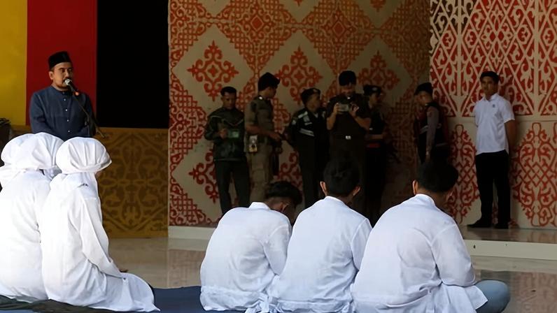 Acehnese people await their turn to receive a public caning during a public caning punishment for violating sharia law in Banda Aceh, Indonesia