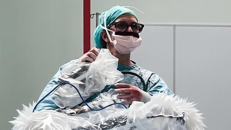 A woman sitting on a log dressed as a mermaid. She is wearing a pink, iridescent tail and a bikini top.