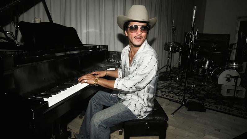 Bruno Mars sits at piano, black and white