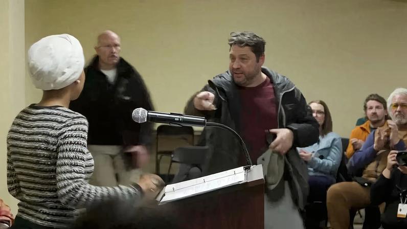 A man shouts at U.S. Rep. Ilhan Omar after spraying her, during a town hall meeting in Minneapolis