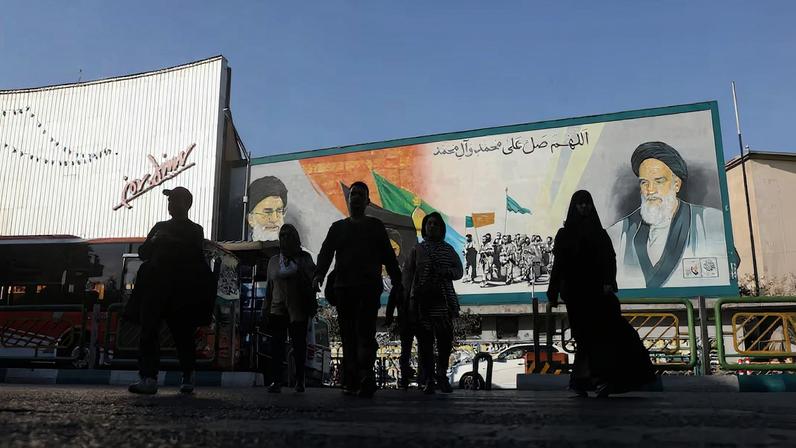 People walk next to a mural with a picture of Iran's Supreme Leader, Ayatollah Ali Khamenei, on a street in Tehran