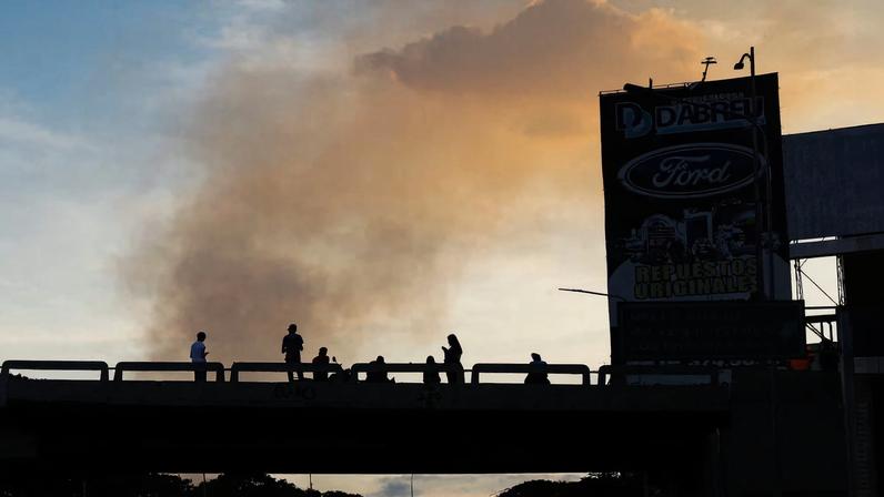 People on a bridge are silhouetted as smoke rises near Fort Tiuna, after U.S. President Donald Trump said the U.S. struck Venezuela and captured its President Nicolas Maduro, in Caracas, Venezuela, January 3, 2026. REUTERS/Leonardo Fernandez Viloria