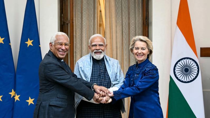 European Council President António Costa, Indian Prime Minister Narendra Modi, and European Commission President Ursula von der Leyen hold hands in front of flags of the European Union and India.