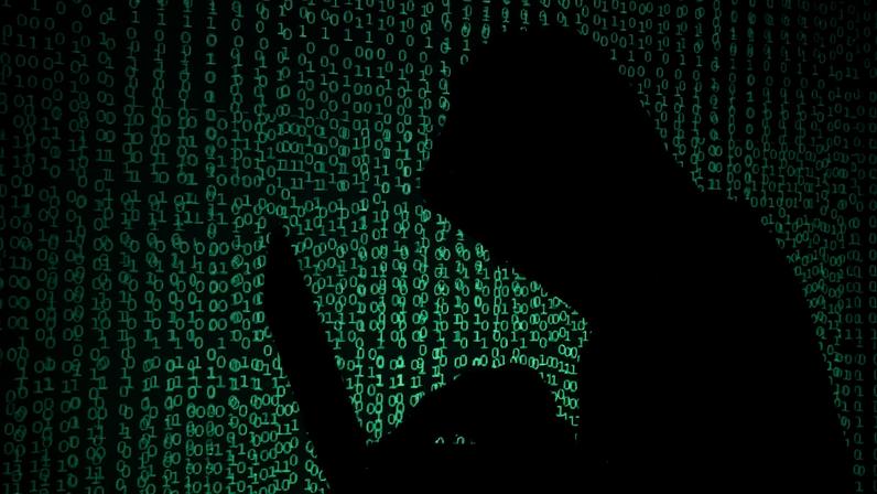 Hooded man holds laptop computer as cyber code is projected on him in this illustration picture taken on May 13, 2017.