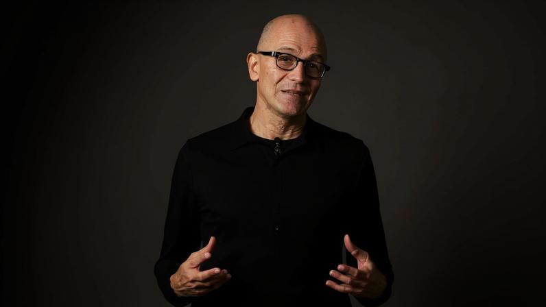 Satya Nadella on a graphic background of the Windows logo.
