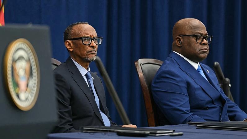 Kagame and Tshisekedi sit side by side at a long desk in front of a dark blue curtain backdrop. Both men wear dark suits and ties.