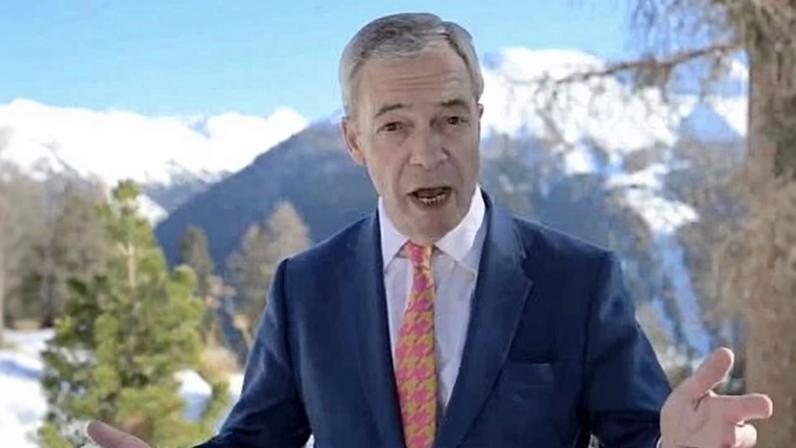 Nigel Farage gesticulating with both hands in front of snowcapped mountains