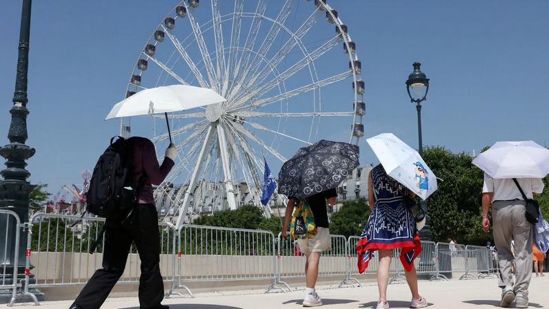 Tourists, holding an umbrella to protect themselves from the sun, walk past a Ferris wheel in the Tuileries Garden on a sunny and warm summer day in Paris as an early summer heatwave hits France, France, July 2, 2025. REUTERS/Tom Nicholson