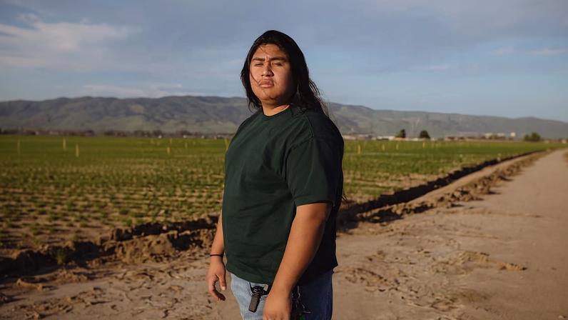 Cesar Vasquez, 18, stands in the fields where his mother and sisters once harvested crops. His work advocating for immigration rights is deeply connected to his family’s immigrant journey.
