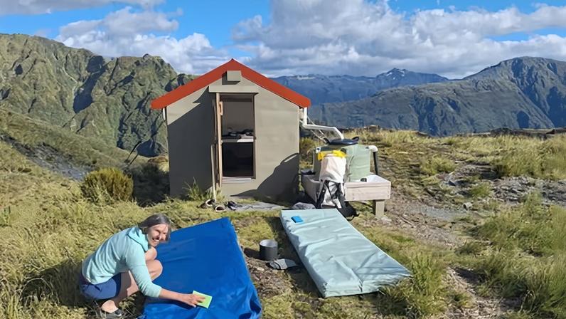 Sonja Risa scrubs mattresses clean at a basic two-bunk hut near Hokitika, New Zealand.