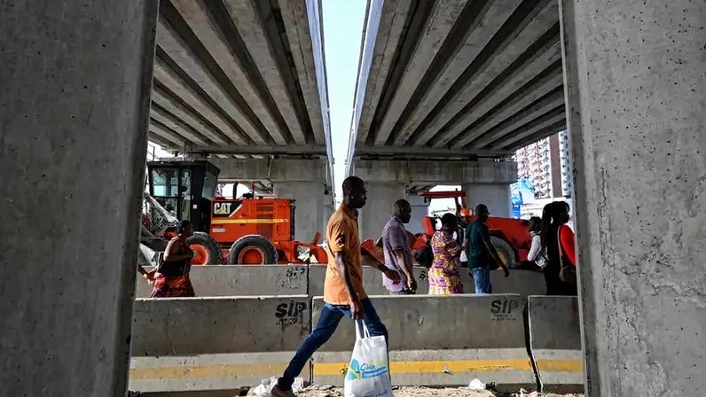 People walk under the construction site of a bridge in the Koumassi commune of Abidjan, Ivory Coast, on May 6, 2025.