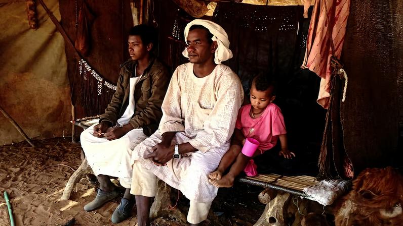 Nomadic herders sitting on a bed made of tree trunks inside their tent, North Kordofan