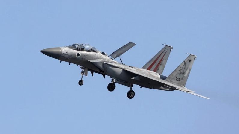 A gray Israeli fighter jet flies against a pale blue cloudless sky.