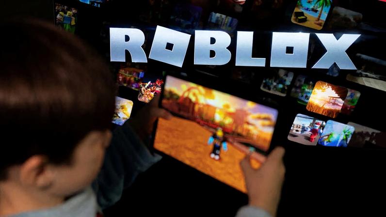 A boy poses for a photo while holding a game pad in front of a screen displaying the logo of the U.S. children's gaming platform Roblox, in this illustration taken December 8, 2025.
