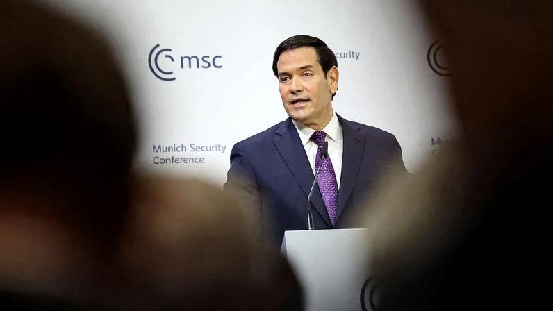 Rubio is shown speaking at a podium ahead of a white background.