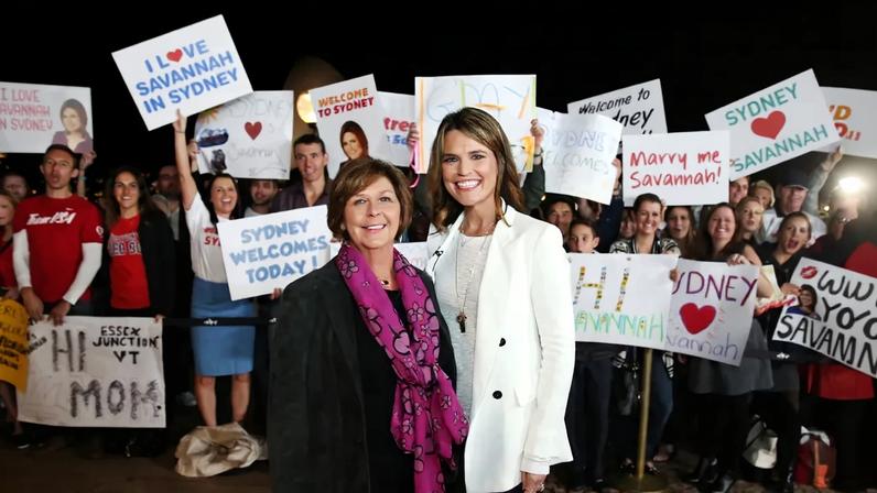 Savannah Guthrie and her mother Nancy Guthrie posing for a photo in front of fans holding signs welcoming and expressing love for Savannah in Sydney.