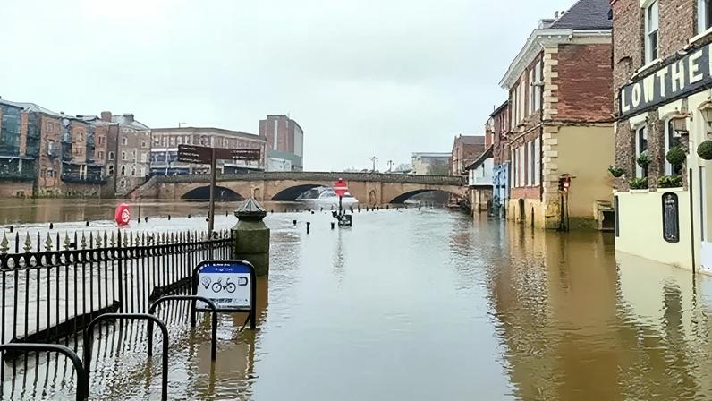 The River Ouse in York flooded over the banks onto the pavement and road with floodwater rising up the side of the buildings.